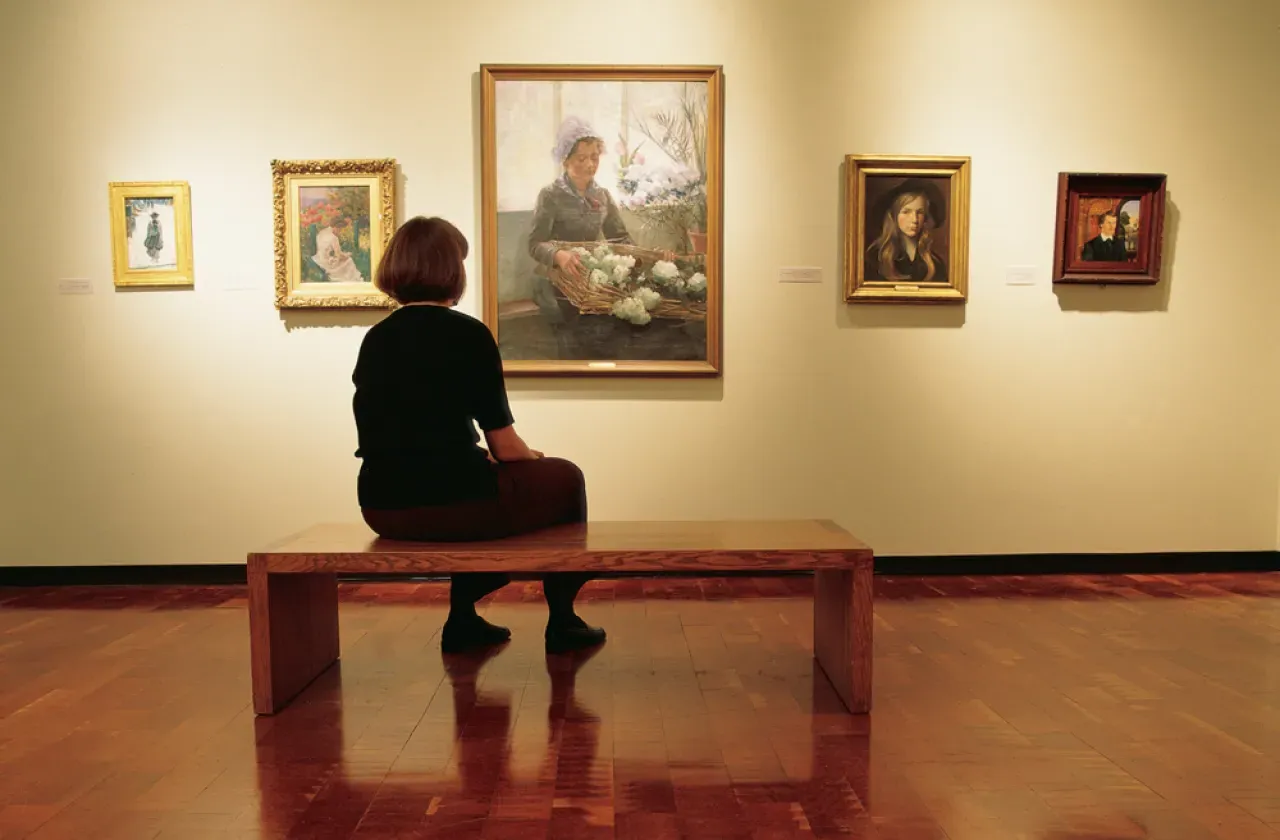 museum goer sitting on a bench taking in a painting of a girl